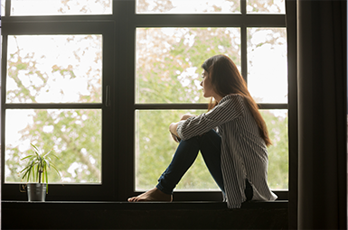 A sad woman sitting on a window sill