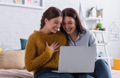 Mom and teenager daughter smiling while looking at a computer screen