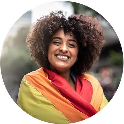 A smiling woman wrapped in a rainbow pride flag