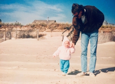 A family photo of the author as a toddler, walking on the beach with her dad