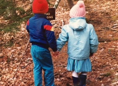 A childhood photo of the author and her brother holding hands on a leafy walk