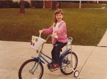 A childhood photo of the author on a bicycle with a basket