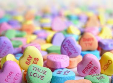 A pile of candy conversation hearts in yellow, purple, blue and green
