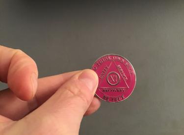 The author shows off a small, round, pink-purple chip she earned in AA
