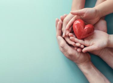Compassion concept image with two pairs of hands holding onto a small, plastic heart
