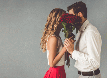 A man and woman hide behind a dozen roses