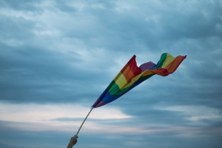 A hand lifting a Pride flag toward the sky. Image courtesy of Yannis Papanastasopoulos
