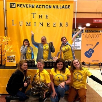A group of seven volunteers in matching yellow t-shirts smile in the Action Village