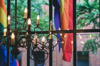 Window with candelabra and pride flag. Photo by Tatiana Rodriguez on Unsplash